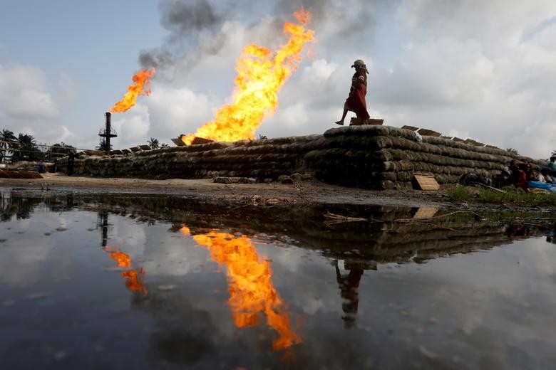 A reflection of two gas flaring furnaces and a woman walking on sand barriers is seen in the pool of oil-smeared water at a flow station in Ughelli, Delta State, Nigeria. REUTERS/Afolabi Sotunde  